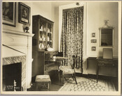 View of a living room in the Homewood estate, including a fireplace, desk, framed portraits, and various pieces of furniture. Homewood was built between 1801 and 1806 as a country home for Charles Carroll, Jr, son of Charles Carroll of Carrollton who was a signer of the Declaration of Independence. The Federal-period Palladian home was…