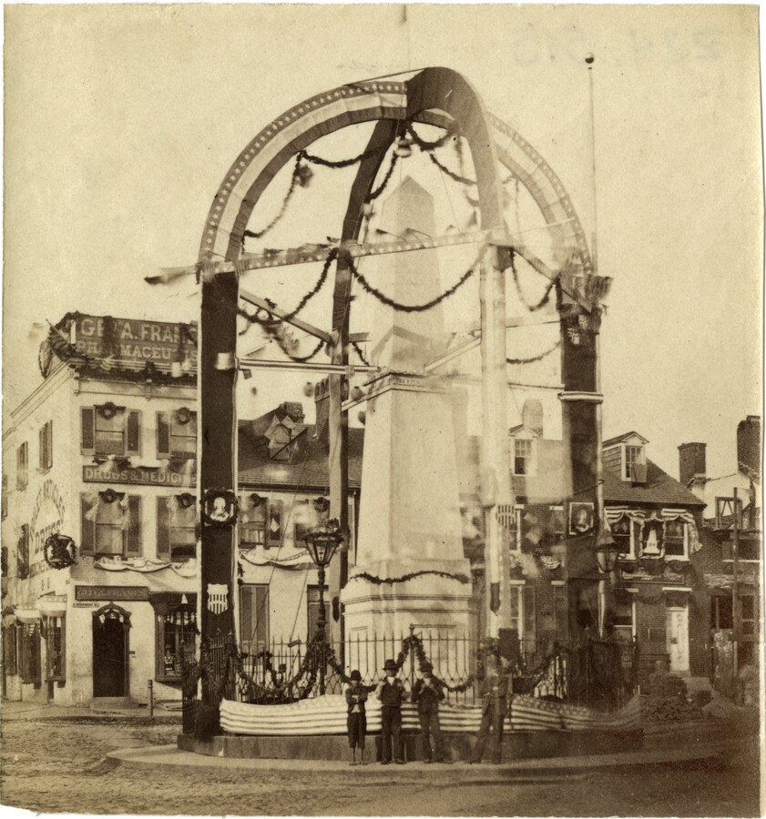 View of the Wells and McComas Monument at East Monument Street and North Aisquith Street in Baltimore, Maryland, decorated for Baltimore's sesquicentennial celebration in October of 1880. The 21-foot-tall obelisk was constructed between 1871-1873 to commemorate Daniel Wells and Henry Gough McComas, two privates in Captain Edward Asquith's Sharpshooters, 1st Rifle Battalion, Maryland Militia. Wells…