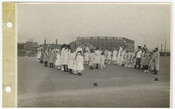 Children form lines to play the game 'King of France.' A waterfront industrial scene is in the background. Verso transcription: Adults supervise children's game, with 'Baltimore and Ohio Rail Road' visible on a building, center right in the background.