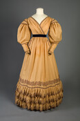 The exuberant and artistic styles of 1830s’ fashion captured the Romantic era’s revival of motifs from the Middle Ages and the Renaissance. Such historic influences can be seen in this dress’s vivid navy blue and apricot color contrast, multi-tiered scalloped hem, and dramatic gigot, or “leg-of-mutton,” sleeves. This dress was worn by Eliza Eichelberger Ridgely…