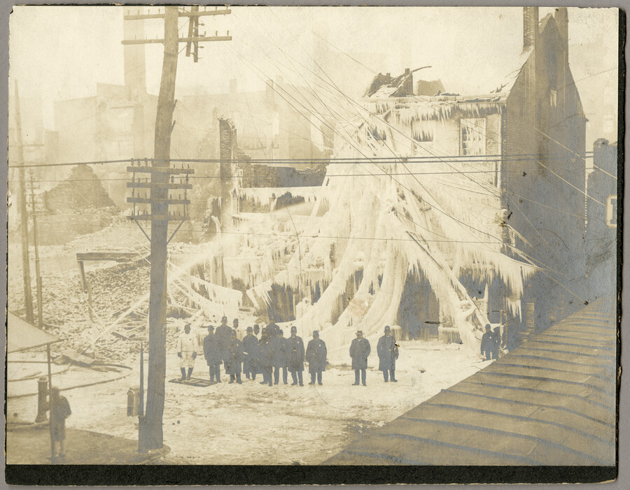 A group of policemen and firemen standing at the northwest corner of Pratt Street and Light Street in front of the ice covered ruins of Anderson & Ireland Hardware after the Great Baltimore Fire of 1904. Because of powder and dynamite stored in the building, it was necessary to keep constant streams of water aimed…