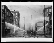 Firefighters fighting the Great Baltimore Fire on the 100-200 block of Liberty Street in Baltimore, Maryland. Multiple firehoses and streams of water can be seen aiming at surrounding buildings.