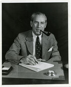 Portrait of Baltimore, Maryland, businessman and social reformer Sidney Hollander seated at a desk with pipe in mouth.
