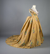 Gold silk taffeta ball gown featuring floral motifs embroidered with blue, lavender, royal purple, gold, orange, pale green, and dark green silk thread. The bodice's neckline and sleeve cuffs are trimmed with silk-net lace.