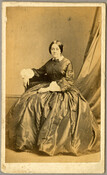 An undated portrait of an unidentified woman. The woman is seated with her hair pulled back and wears a dress that features a large skirt and frilled cuffs. Verso transcription: Charles D. Fredericks & Co., "Specialité," 867 Broadway, New York