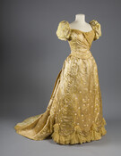 Gold and pale yellow silk satin and silk brocade evening dress embellished with netting and lace by the House of Worth. The silk brocade features a green and pink floral pattern. Dress comprises of a bodice and a skirt with a detachable train.