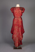 Evening dress constructed from red silk brocade with gold floral motif. Left shoulder decorated with a three-dimensional silk brocade rose. Dress has a matching belt and the skirt is tailored and cut to create the skirt's unique shape.