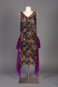 While 1920s’ fashion is probably best known for short, spangled evening dresses, their popularity was brief. The purple crêpe foulards, or scarves, attach at the dropped waist line of this dress and hang well below its knee-length skirt, giving a nod toward the revival of floor-length evening gowns that became stylish in the 1930s.