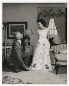 Wallis Simpson, Duchess of Windsor, wears an evening gown known as the "Monkey Dress," designed by French couturier Givenchy. Prince Edward, Duke of Windsor, kneels in front of her.
