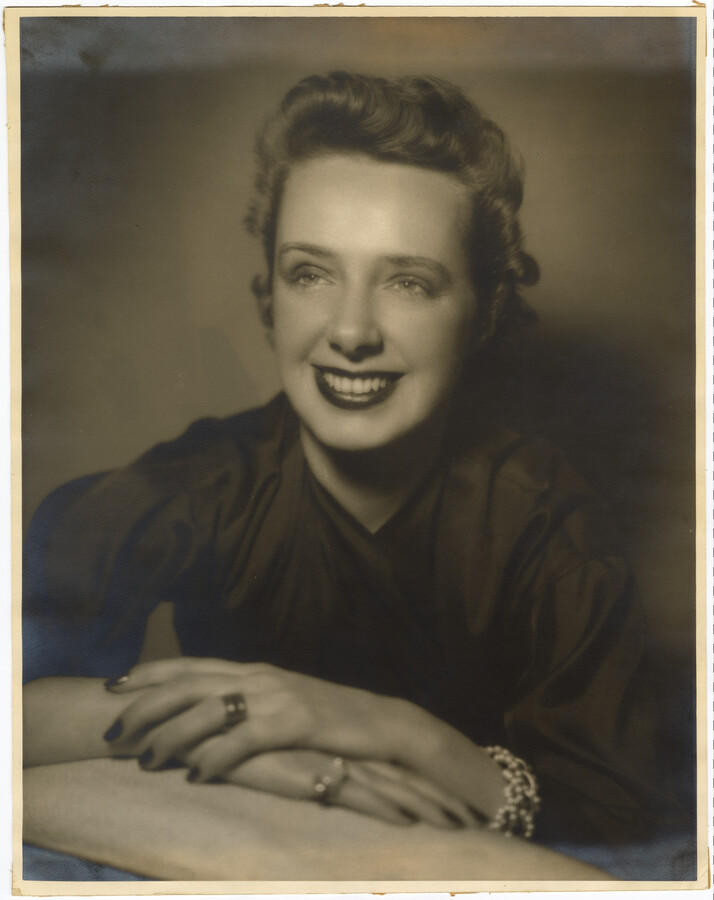 A portrait of American fashion designer Claire McCardell seated with her hands placed in front of her.
