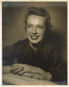 A portrait of American fashion designer Claire McCardell seated with her hands placed in front of her.