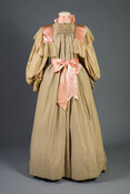 Beige tea gown trimmed with long bishop sleeves and lace and pink satin ribbon with a Watteau back.