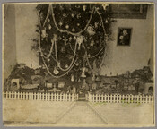 Photograph of a Christmas garden most likely made by the photographer, Van Buren Davis. The garden includes a decorated Christmas tree along with tracks for a toy train.
