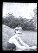 Photograph of American fashion designer Claire McCardell wearing glasses and a strapless outfit while sitting on the ground.