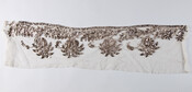 Fragment of muslin embroidered with silver metallic thread in shape of pineapples or palm trees. Probably intended for use on the hem or trim of a dress.