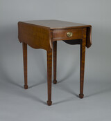 A Hepplewhite-style, tiger grain mahogany, drop-leaf Pembroke table by Enrico Liberti, the eminent master cabinet maker of Baltimore, Maryland. The table features square tapered legs with spade feet, butterfly leaf supports, a serpentine molding edge top, and oak and poplar secondary wood. There is a single drawer to the end of the table with a…