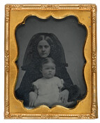 A cased ambrotype portrait of 14-month-old Louisa R. Coolidge and a woman presumed to be her mother. The child is dressed in a white dress and sits in the lap of the woman who is wearing a black dress and veil.