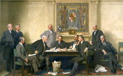A large group portrait of ten men around a table, six seated and four standing. The table is covered in papers with a wastebasket beneath it. Behind the men, above a fireplace, is a mural featuring the Maryland flag with the word "Fidelity" above it.