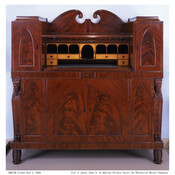 Baltimore Empire cylinder desk made with mahogany and satinwood. Desktop with two gothic-panelled side cabinets, scroll pediment over cylindrical closing. Interior of pigeon holes, small drawers, and writing surface. Bottom cabinet contains corner columns of Saracen's' heads on tapered columns carved with acanthus leaves, and carved feet.