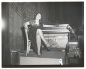 Unidentified performer, possibly a vocalist, seated at an organ and smiling.