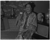 Photograph of an unidentified woman holding a glass of Arrow Beer with the empty bottle beside her. Possibly a promotional photograph for Arrow Beer.