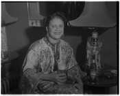 Portrait of an unidentified woman holding a glass of Arrow Beer. The empty bottle sits on a table beside her. The image is possibly a promotional photograph for Arrow Beer.