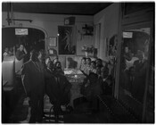 Charles Law and company posing for a photograph during social hour in a large restaurant booth. Charles Law was a prominent funeral director whose funeral home was located at 802 West Madison Avenue in Baltimore, Maryland. A sign stating "Please do not use profanity" hangs behind the group in the archway.