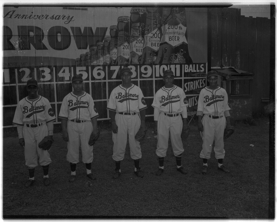 Group portrait of five pitchers of the Elite Giants, a Negro League baseball team from Baltimore, Maryland. From left to right: Ed Finney, Frank Russell, Lenny Pearson, Jim Gillain, and Thomas "Pee Wee" Butts. Behind them is a scoreboard and advertisement celebrating the 200th anniversary of Arrow Beer.