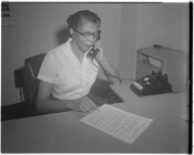 An unidentified woman sitting at a desk and speaking into a telephone.
