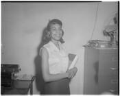 An unidentified woman smiles while holding a book in an office setting.