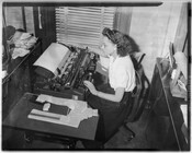 Photograph of an unidentified woman seated at a desk with a typewriter, transcribing documents.