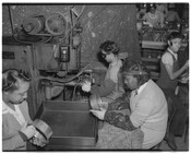 Four factory employees, possibly World War II defense workers, at work on machines.