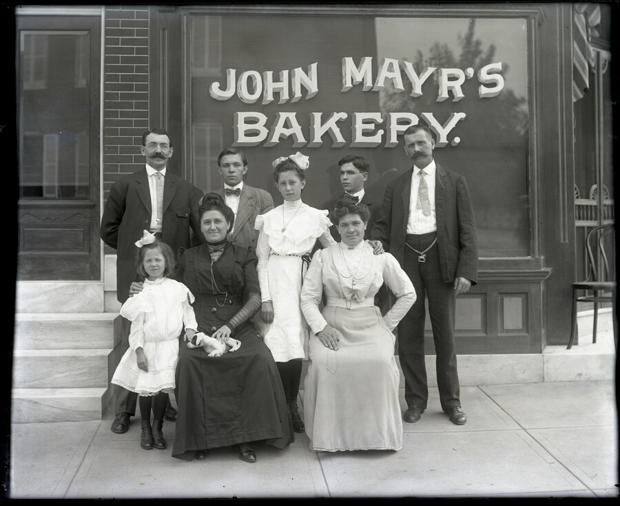 Portrait of a group, presumably the Mayr family, posed in front of John Mayr's Bakery. The bakery was located at 839 North Wolfe Street, Baltimore, Maryland.