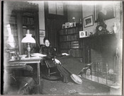 Ellen L. Duvall Steuart in her home at 123 West Lanvale Street, Baltimore, Maryland. Mrs. Steuart leans back in a rocking chair beside a fireplace, holding a banjo in her right hand.
