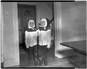 Two smiling children in costumes possibly dressed for Halloween. They appear to be standing in the interior of a home.