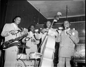 Promotional photograph for Arrow Beer featuring the Flink Johnson Combo. Members include Flink Johnson on the right; Charlie Fletcher on bass; and "Pigmeat" Garner on saxophone. A fourth member is unidentified. All men are on stage holding bottles of Arrow Beer.