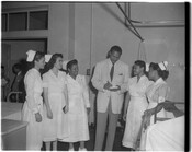 A group of five nurses standing beside a doctor, possibly at Provident Hospital in Baltimore, Maryland. The nurses are looking at the doctor and smiling as he writes on a pad of paper.