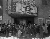 Street scene of a crowd in front of the Apex Theatre. The theatre was located at 110 South Broadway, Baltimore, Maryland. A large group of children is gathered under the marquee, which advertises Liane Jungle Goddess and Rodan.