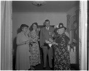 Maryland Governor Theodore McKeldin standing with three unidentified women in a living room. Two of the women are holding plates of food. Behind the group is a table with food and drinks.