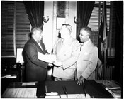 Baltimore, Maryland, Mayor Thomas D'Alesandro, Jr presenting a document to and shaking hands with Dr. Bernard Harris. An unknown man stands to the right watching the interaction.