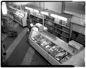 Interior view of grocery store, as seen from the upper floor. The meat case is shown to the right with several other shelving units along the far wall of the store.