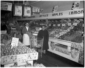 Interior view of an unidentified grocery store with customer and employee standing in the produce section.