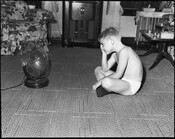 View of a boy seated in front of an electric fan on the floor of a living room.