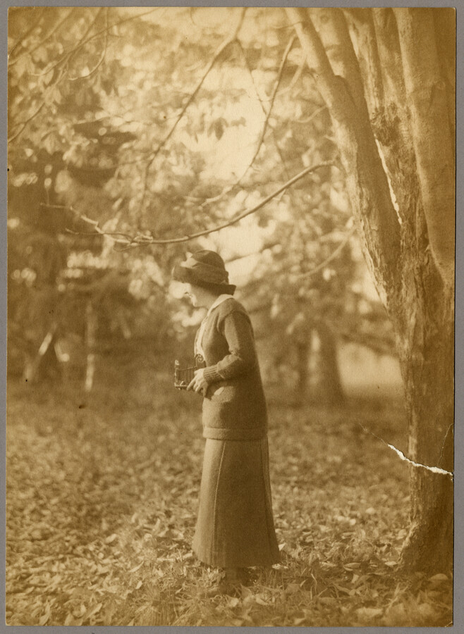 Ruth Hayden (Wanzer), daughter of Baltimore, Maryland, photographer Emily Spencer Hayden, holding a camera while standing under a tree.