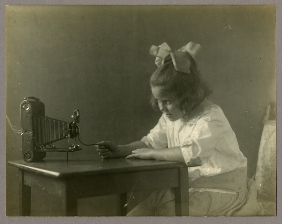 A Photograph of Anna Bradford Hayden, nicknamed "Nan," seated at a table with a camera's shutter release in her hand. She was the daughter of Baltimore, Maryland, photographer Emily Spencer Hayden.