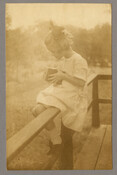 Photograph of Baltimore, Maryland, photographer Emily Spencer Hayden's daughter Anna Bradford Hayden, also known as "Nan," seated on a fence and peering into the viewfinder of a camera.