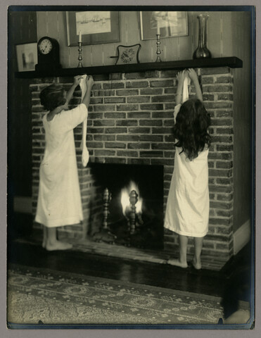 Nan and Dot hanging stockings at living room fireplace — circa 1912