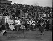 The Homecoming court, adorned with sashes and flowers, sits on a bandstand in front of a packed crowd at Morgan State College.
