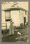 Portrait of Anna Mullikin with dog in front of the small stone house behind the home of Baltimore, Maryland, photographer Emily Spencer Hayden. Verso transcription: Anna Millikin. Boy (Dog). Old stone house behind Hayden home in Catonsville. Oldest stone house in MD? Nan and Pat lived here.