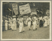 View of women from the Just Government League of Maryland marching in Columbus, Ohio. The women march down the street holding signs that read "Votes for women / Just Government League" and "Just Government League / Liberty or death / Don't tread on me." The sidewalk is full of onlookers, and storefronts and signs are…
